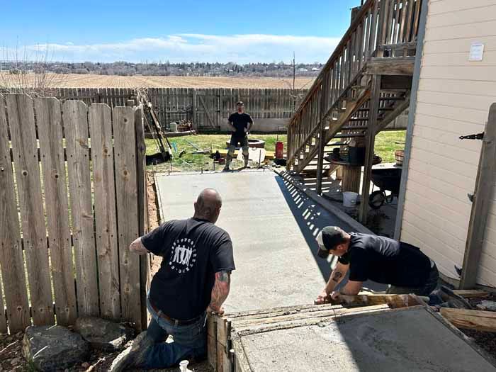 Three people working on a concrete project outdoors near a fence and stairs.