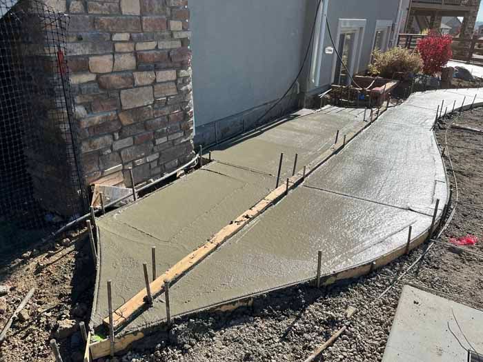 Freshly poured concrete walkway next to a stone wall and a light-colored house.