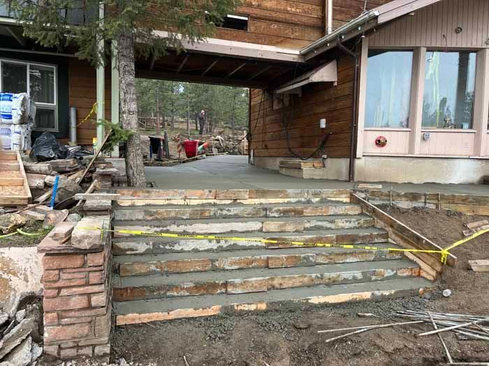 Stone steps under construction at a wooden house. Yellow caution tape and concrete visible.