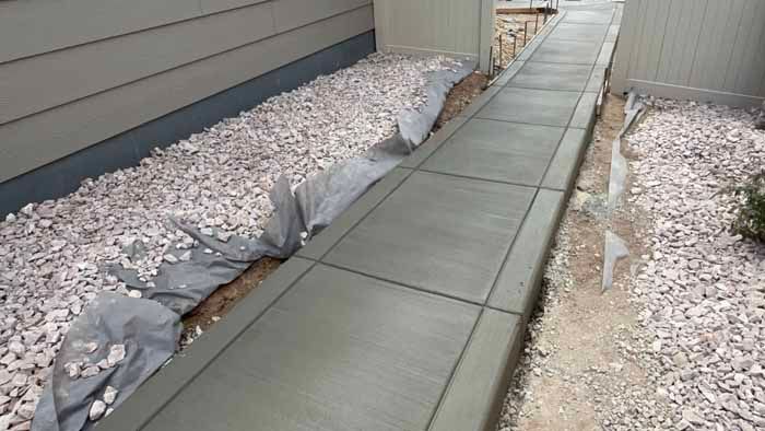 Concrete walkway alongside a house, gravel bed on one side.