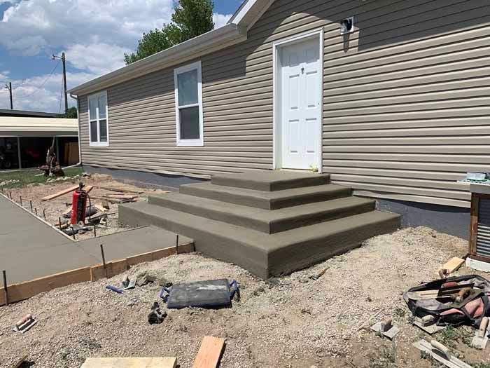 Concrete steps leading to a house entrance; concrete sidewalk under construction.