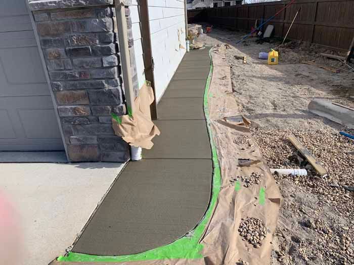 Freshly poured concrete sidewalk next to a house under construction.