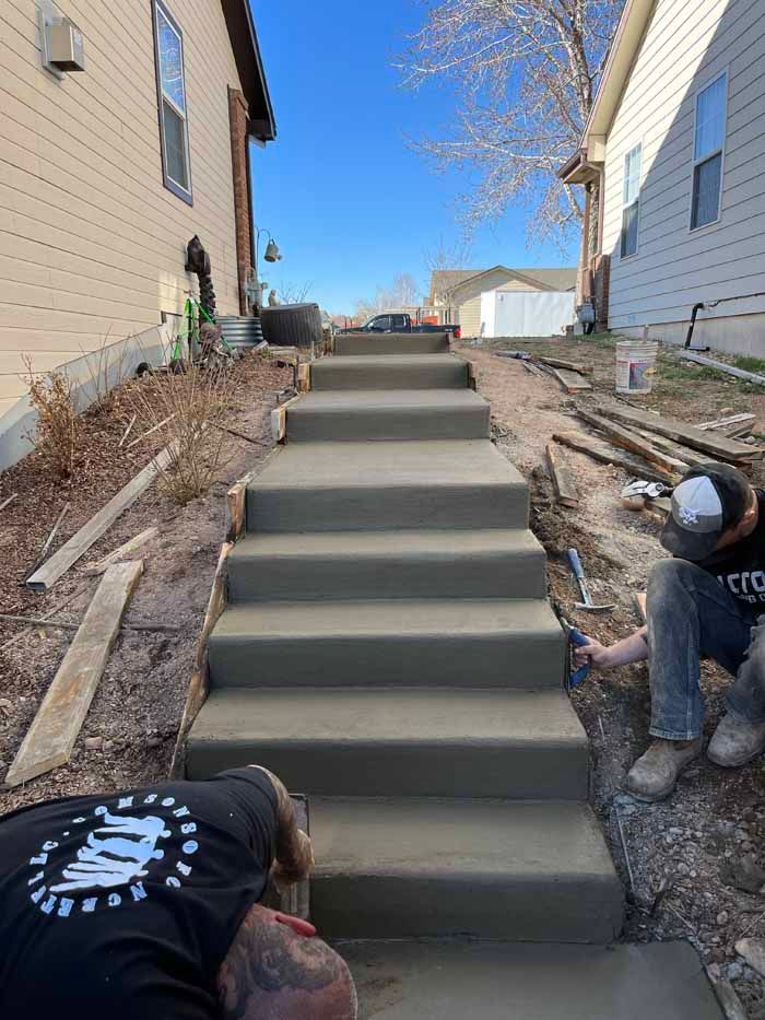 Concrete steps under construction between two houses. Two workers finishing the steps on a sunny day.