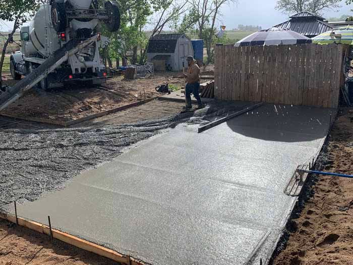 Concrete being poured and leveled for a patio with a worker. Truck in the background.