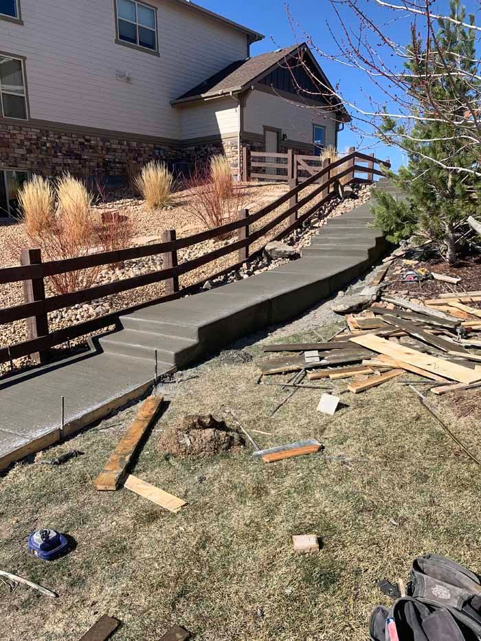 Newly poured concrete walkway and steps leading up to a house with a wooden fence alongside.