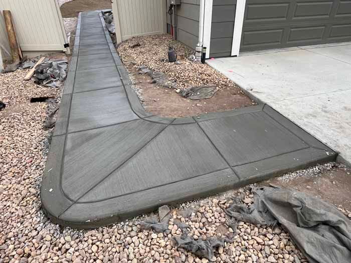 Freshly poured concrete sidewalk and ramp, curving to a garage.