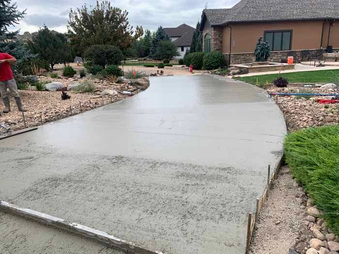 Freshly poured concrete driveway in front of a house, with workers in the background.