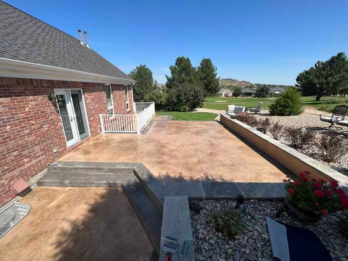 Brick house with a stamped concrete patio, steps, retaining wall, and landscaping under a clear blue sky.
