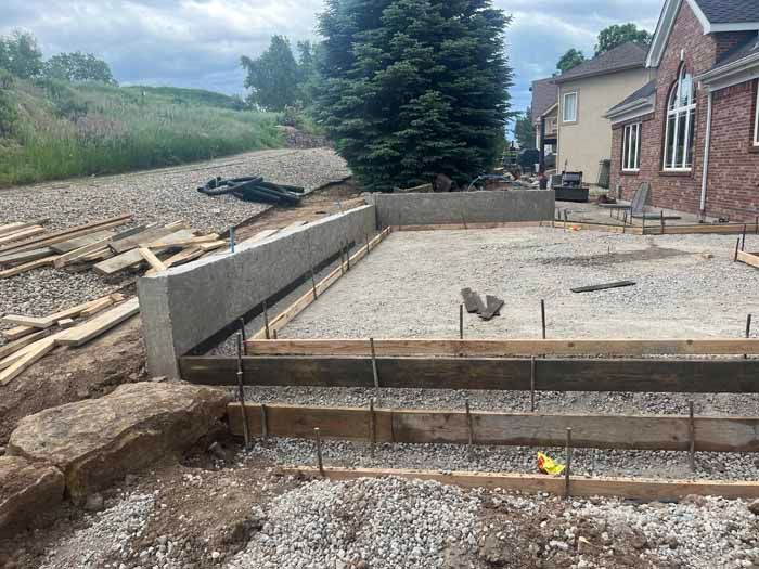 Construction site with concrete foundation and gravel base near a brick house.