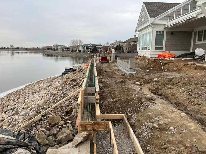 Construction of a retaining wall along a lakefront, with concrete forms and rebar visible.