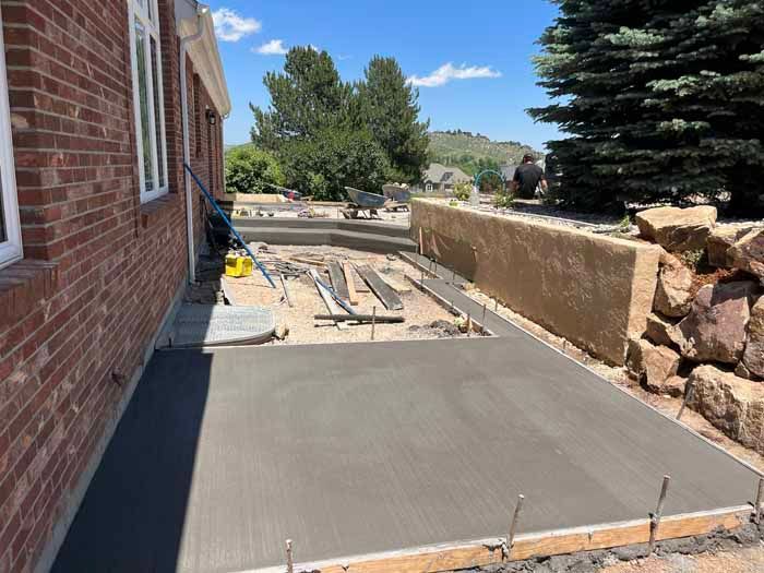 Newly poured concrete patio next to a brick building. Construction materials and landscaping are visible.