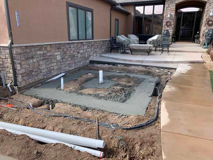 Concrete poured for an in-ground structure, possibly a hot tub, near a house with stone accents.