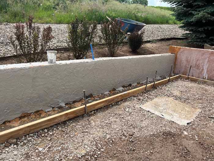 Concrete retaining wall under construction in a gravel yard, with rebar and wooden forms.