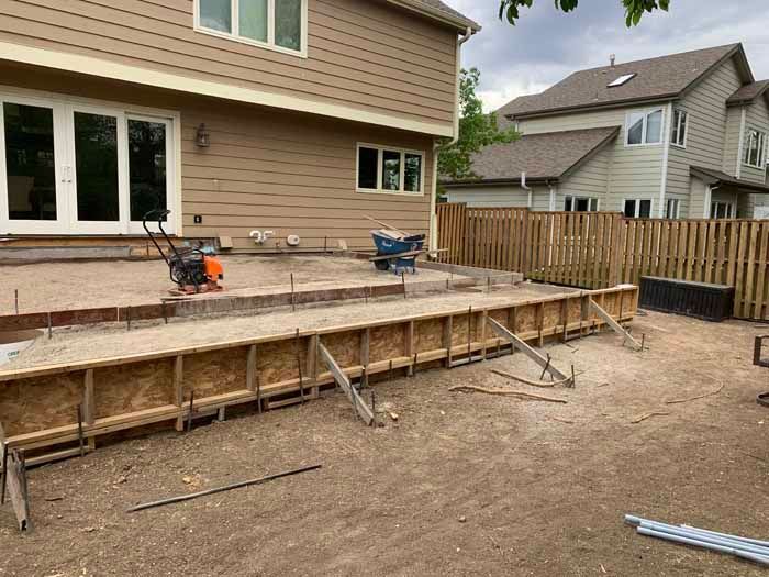 Construction site; forms for a concrete patio are built in a backyard next to a house with a wooden fence.