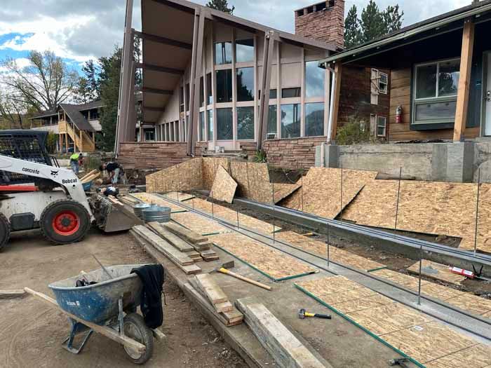 Construction site with a building, plywood, lumber, a bobcat, and a wheelbarrow.