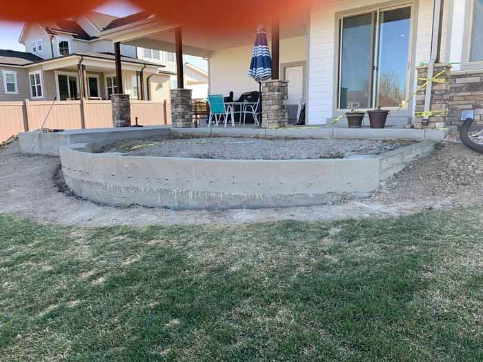 A curved concrete patio border under construction; part of a house and yard visible.