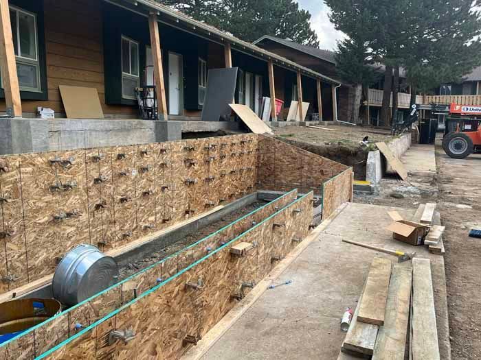 Construction site with wooden forms and concrete work in front of a building with cabins.