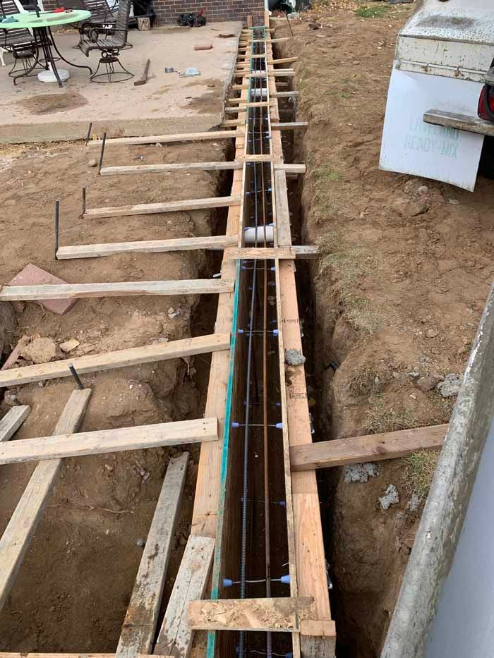 Wooden formwork for concrete foundation with rebar reinforcement in a trench.