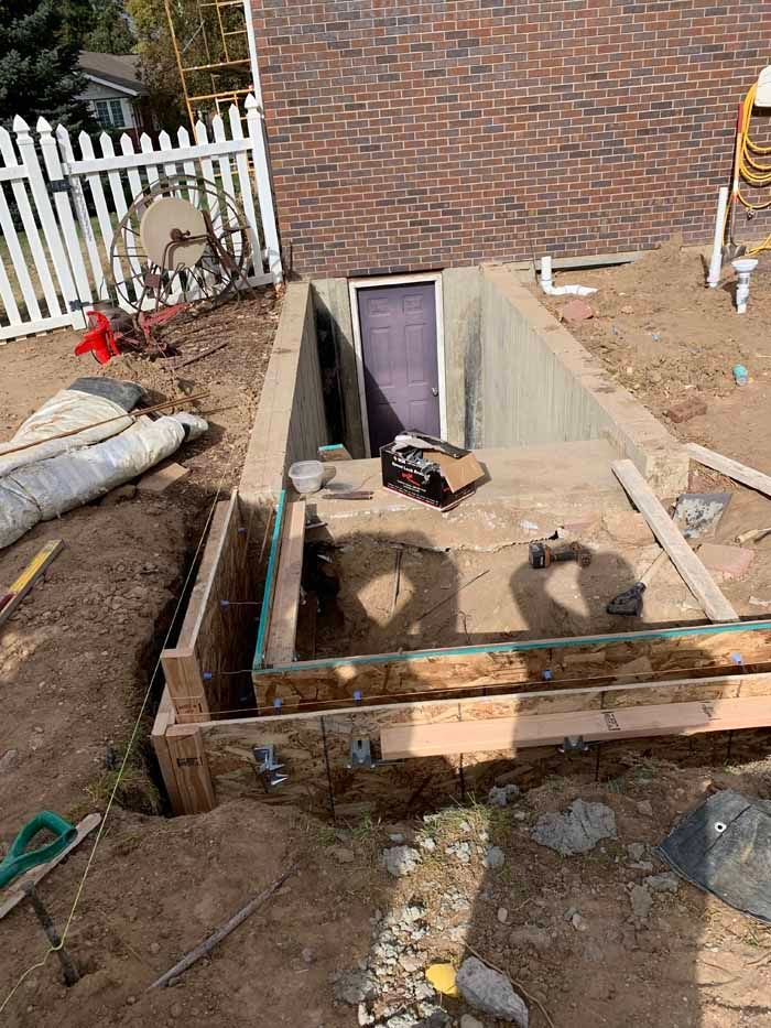 Construction of a concrete cellar entrance with a door, surrounded by wooden framing and soil, outdoors.