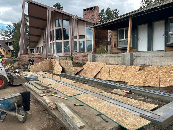 Construction site with wooden forms and building materials in front of a multi-story building.