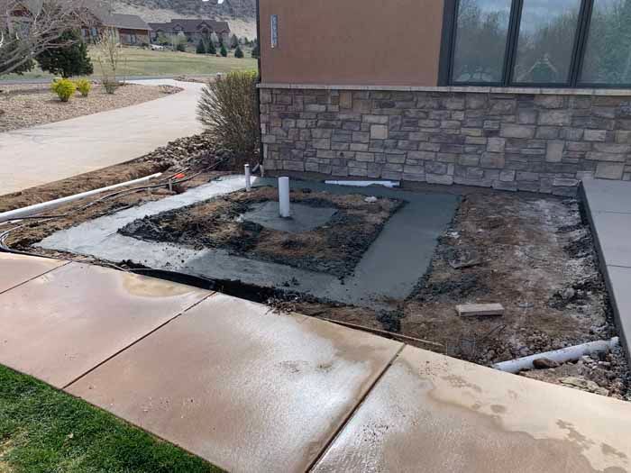 Concrete work in progress beside a building, with sidewalk, soil, and pipes visible.