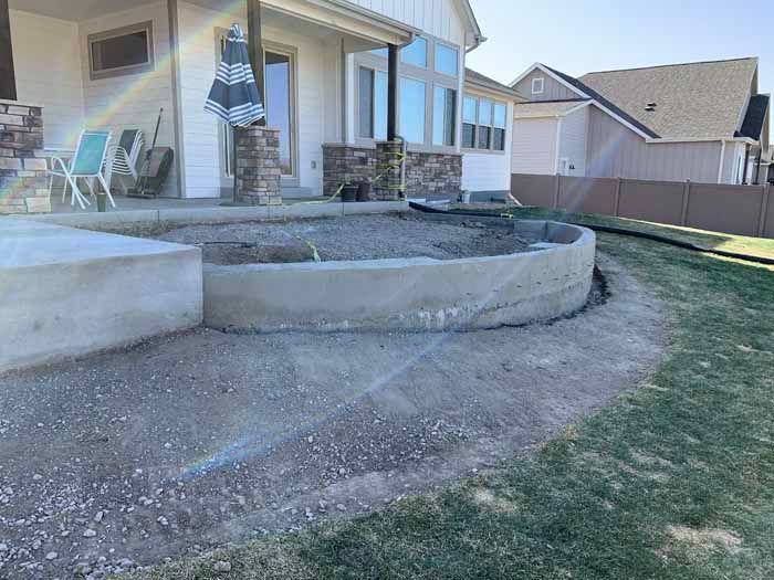 Concrete patio with curved border, gravel inside, next to grass and house.