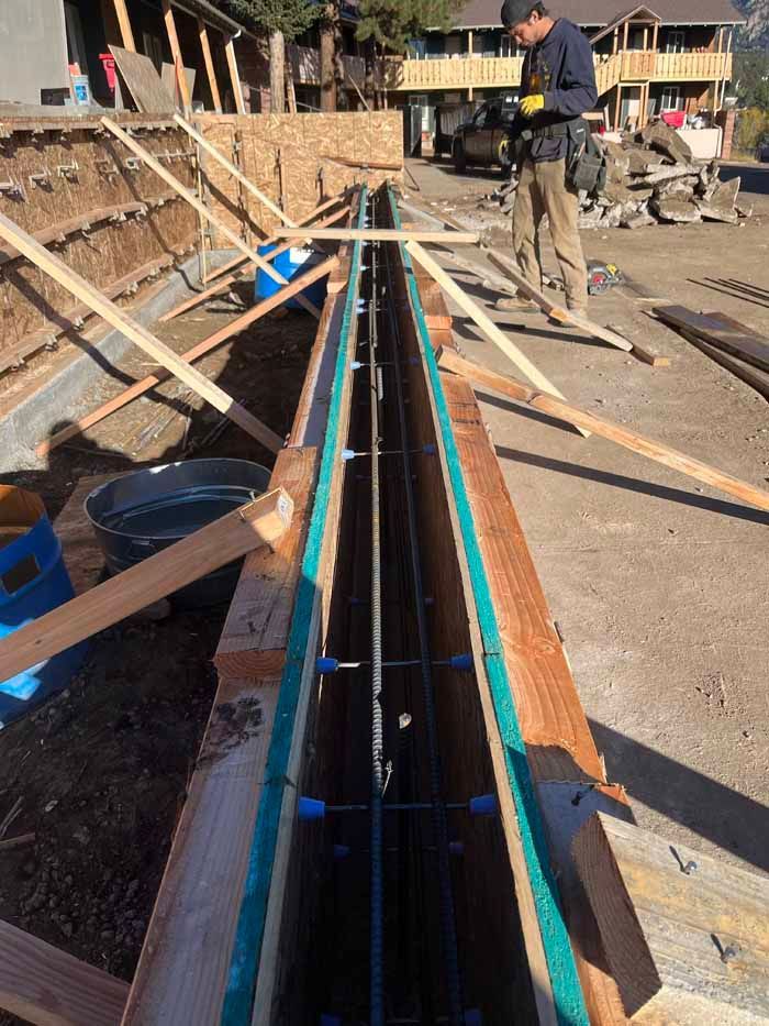 Construction site: Wooden forms for concrete work, rebar reinforcement in place. A person inspects the forms.