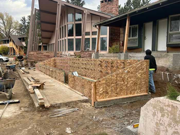 Construction site with wooden forms for a retaining wall in front of a house. Workers are present.