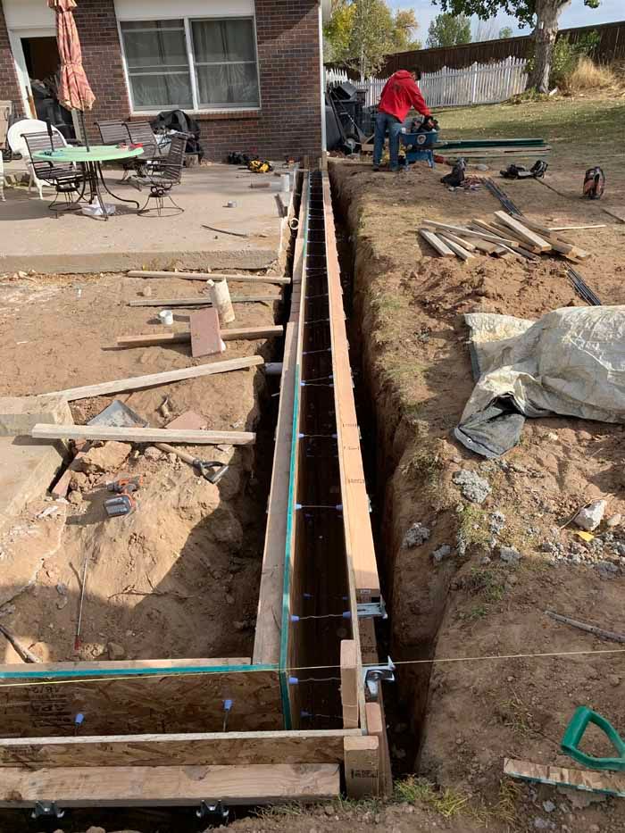 Construction site: Wooden forms for a concrete structure, trench dug in dirt, person in red shirt working.