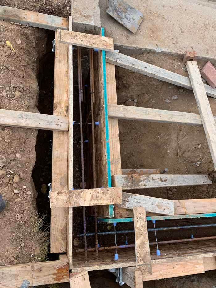 Wooden forms and rebar frame a trench, prepared for concrete pouring.