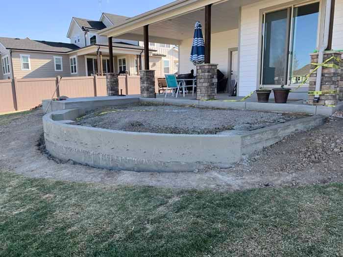 Curved concrete patio border under a covered porch with a gravel interior, on a grassy lawn.