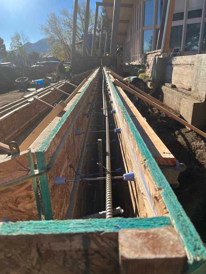 Wooden forms prepared for concrete, with rebar visible, set against a building.