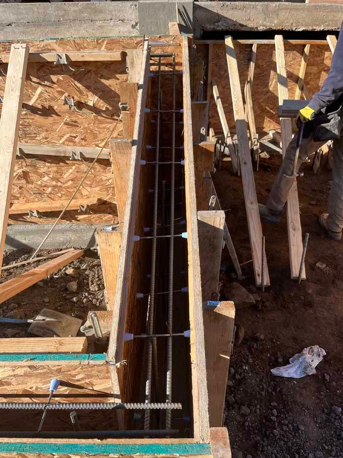 Wooden forms for a concrete footing with rebar inside, construction site setting.