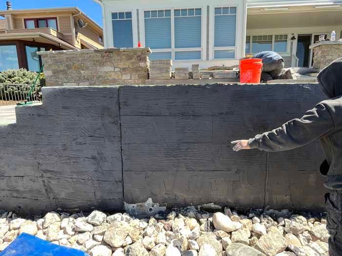Man pointing at a newly constructed retaining wall with textured grey concrete and stone.