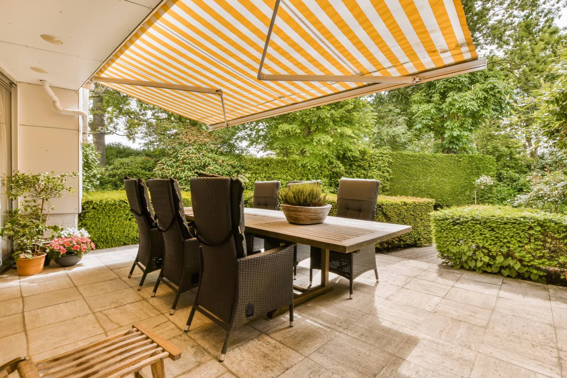 A retractable awning with white and yellow stripes, covering an outdoor dining table and chairs