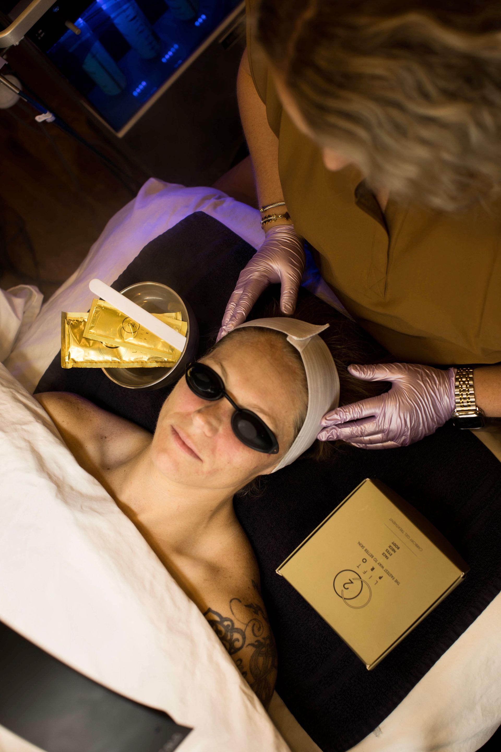 A woman wearing sunglasses is getting a treatment on her face.