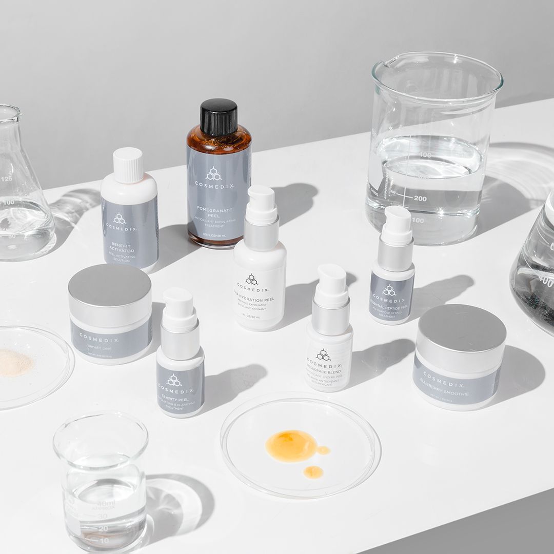 A table topped with bottles of cosmetics and a beaker of water.