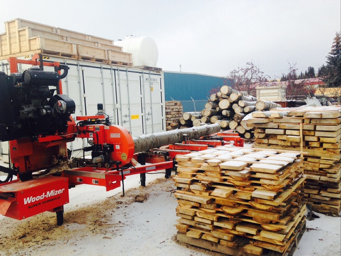 Log splitter beside stacked lumber and logs in a snowy lumber yard