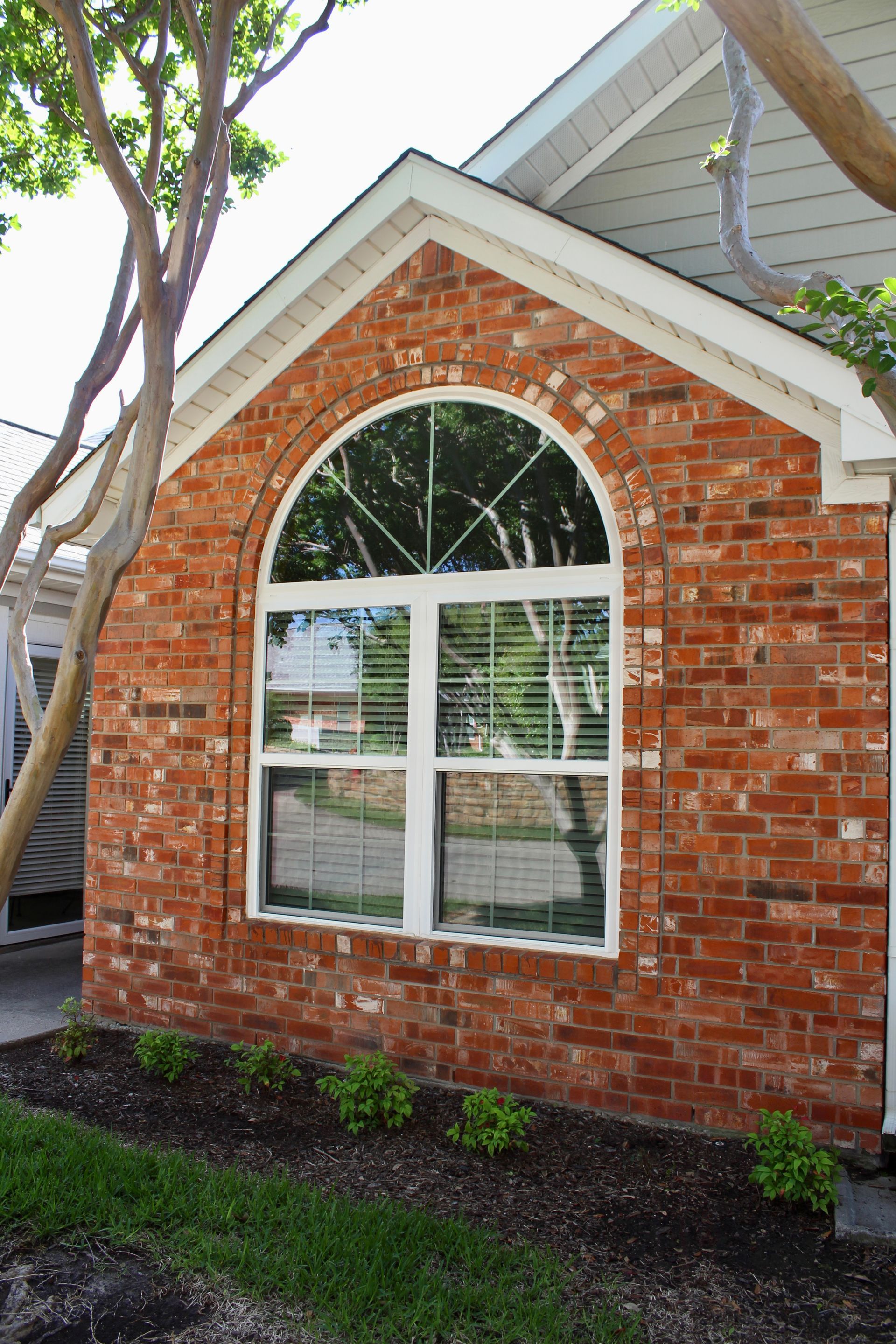 A brick building with a white window and a tree in front of it.