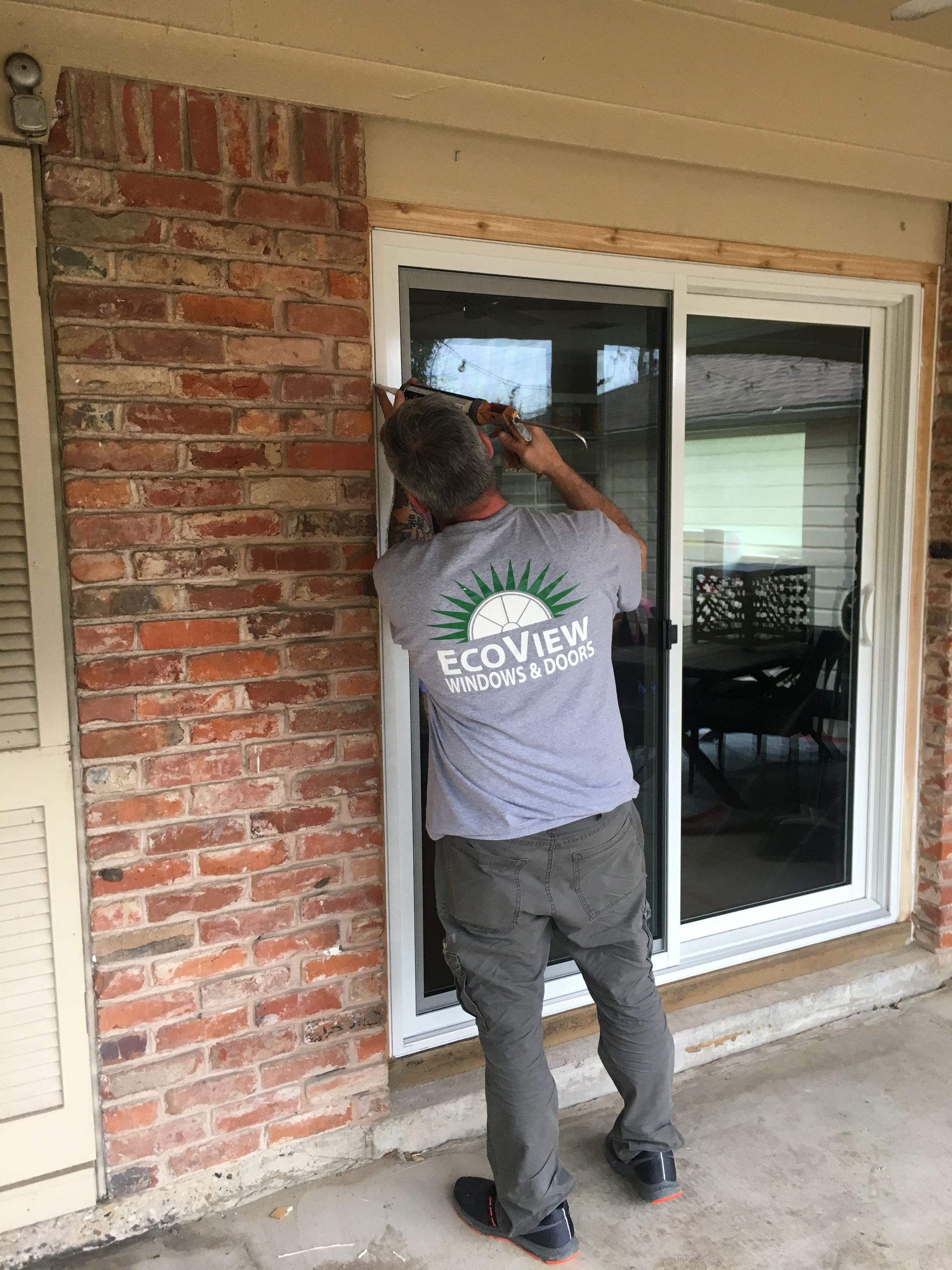 A man is installing a sliding glass door on a brick wall.
