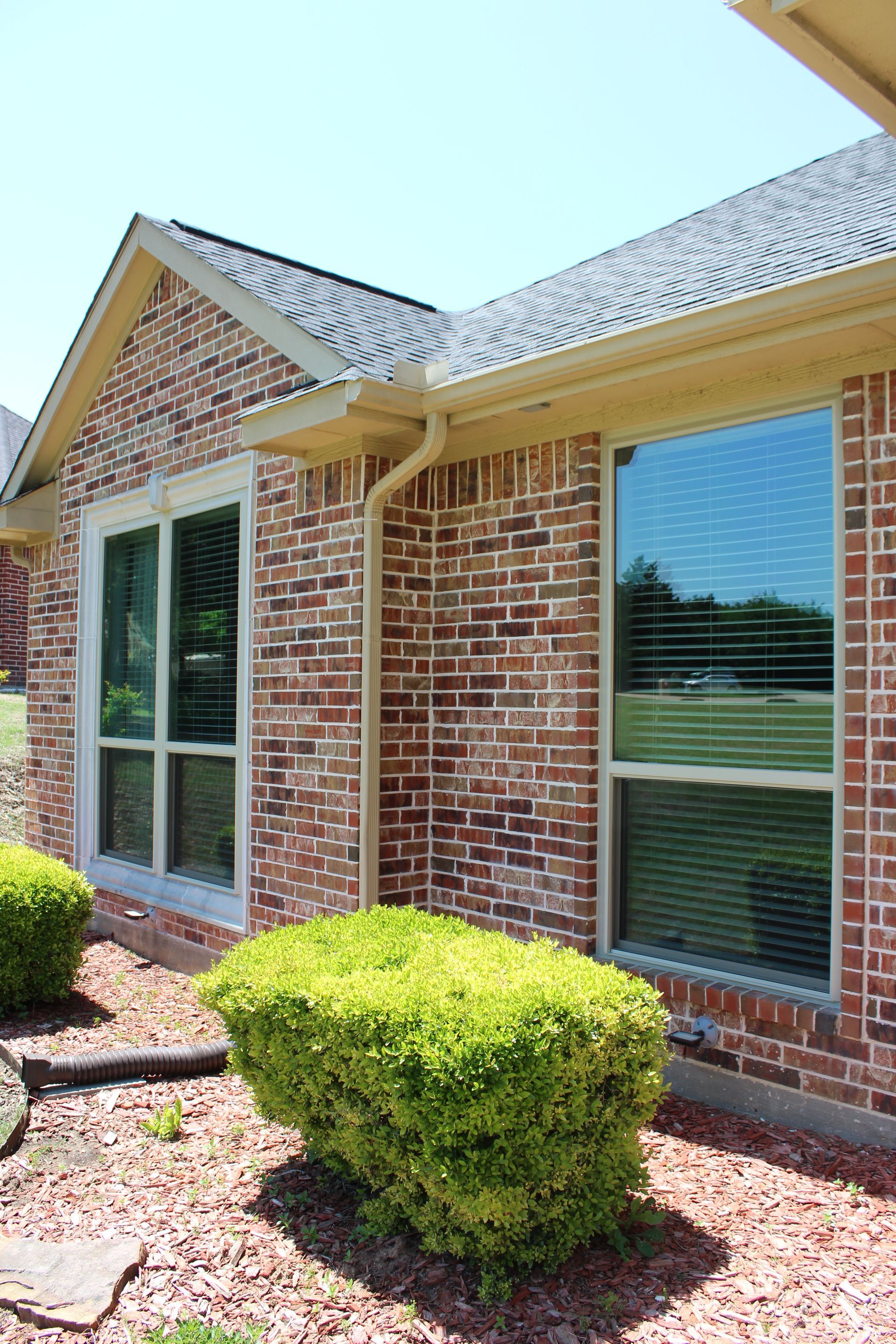A brick house with a lot of windows and bushes in front of it.