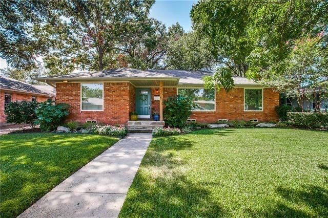 A brick house with a lush green lawn and trees in front of it.