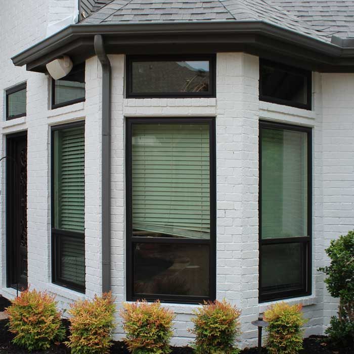 A white brick house with a bay window and black blinds
