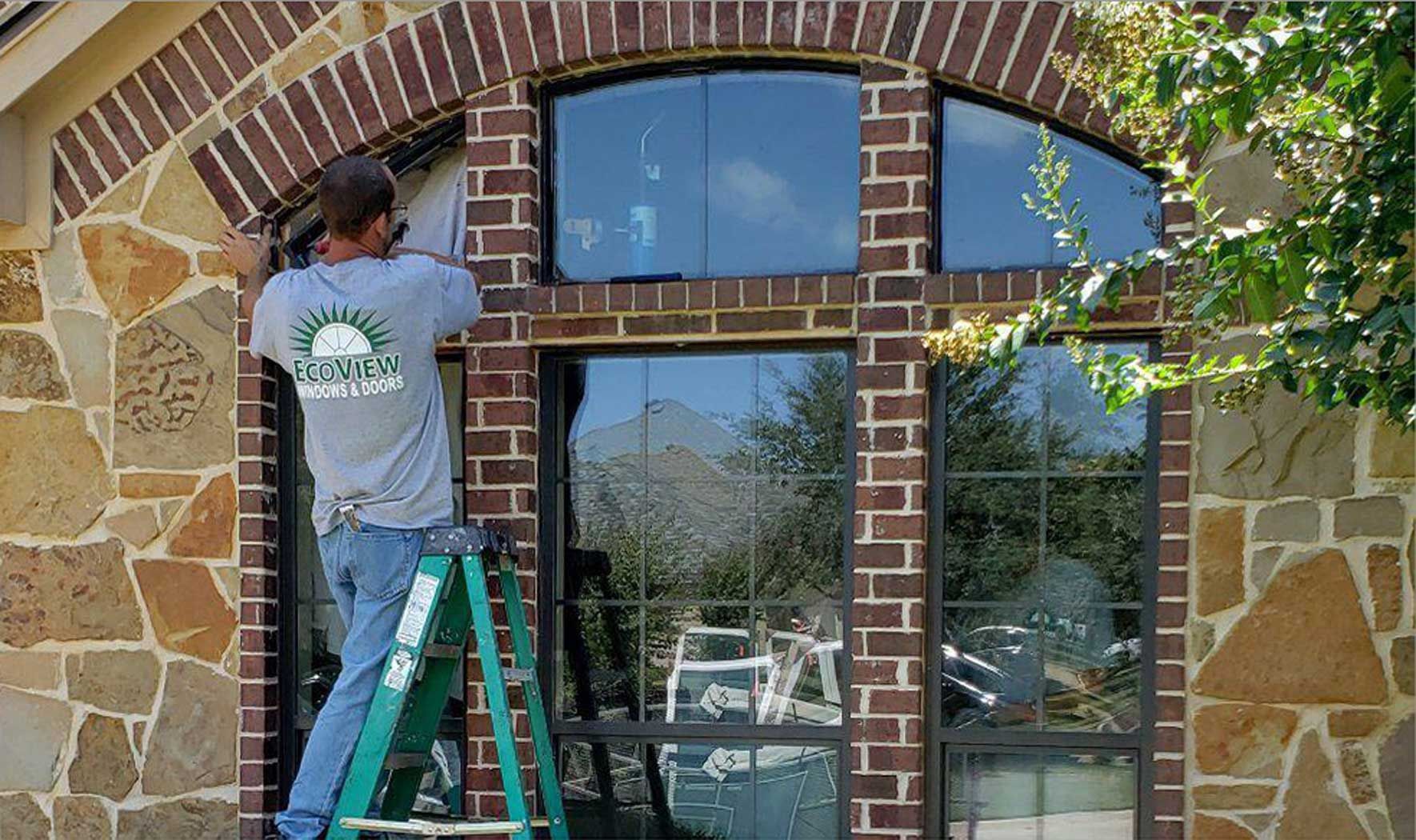 A man on a ladder is installing a window on a brick building.