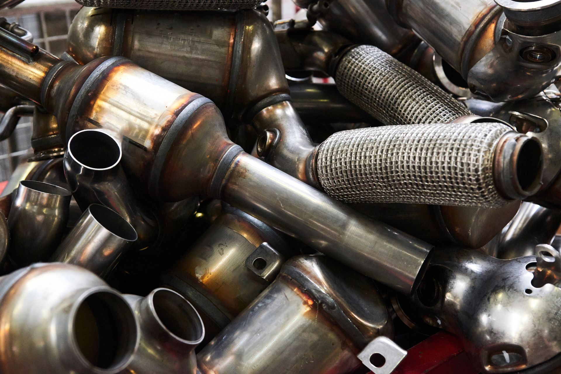 Pile of used catalytic converters, mostly silver metal with welded joints and exhaust connections.