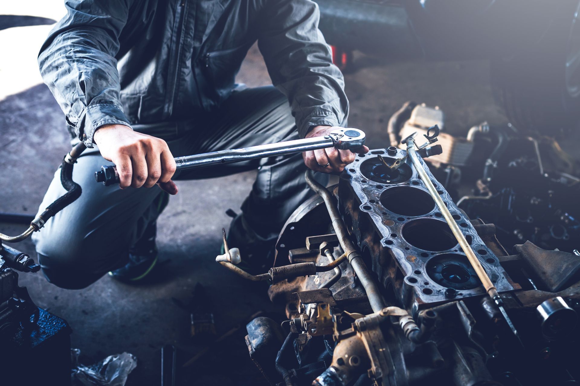 Mechanic working on car engine with wrench in a dimly lit garage.