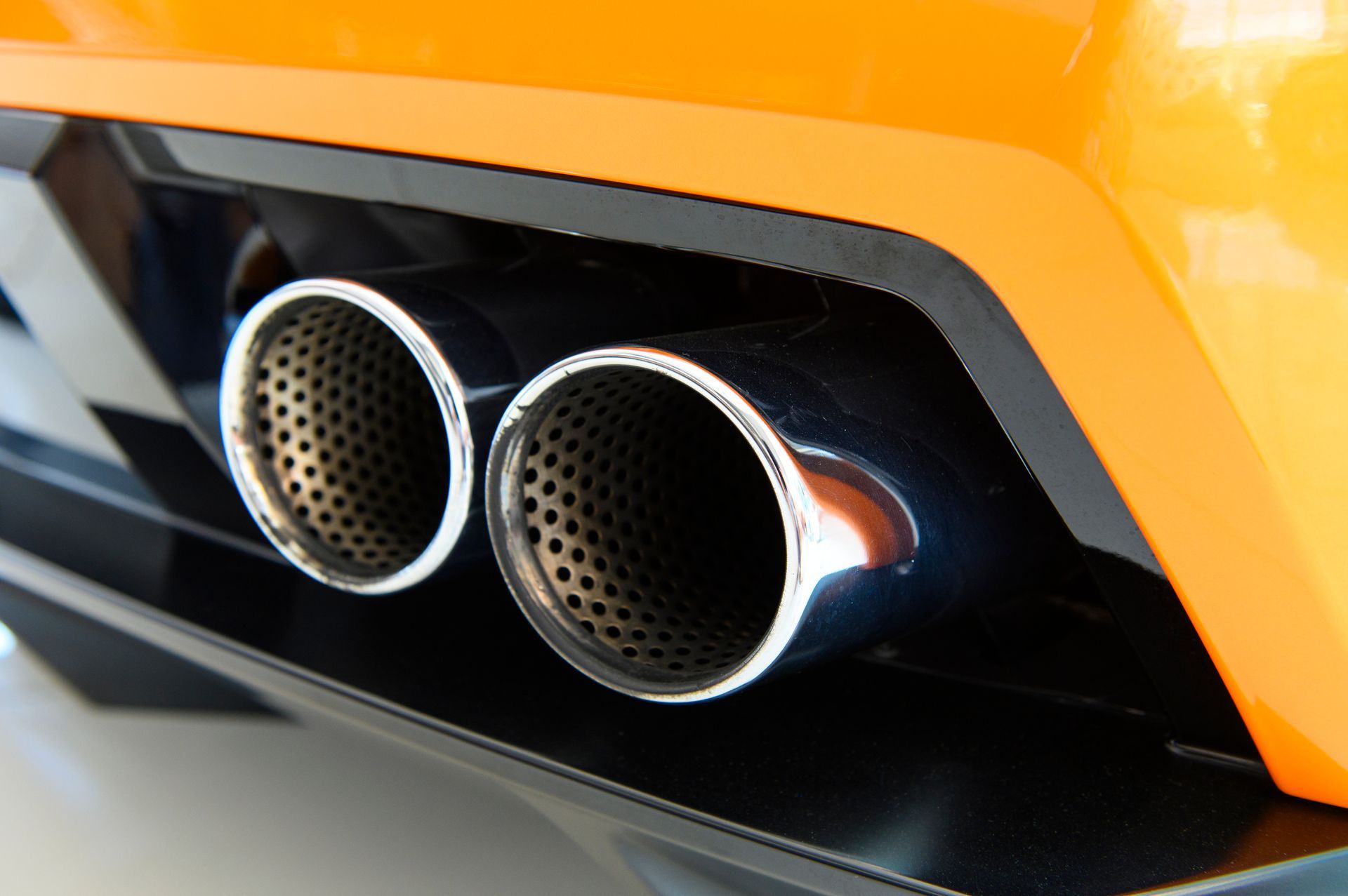 Two chrome exhaust pipes on an orange car bumper.