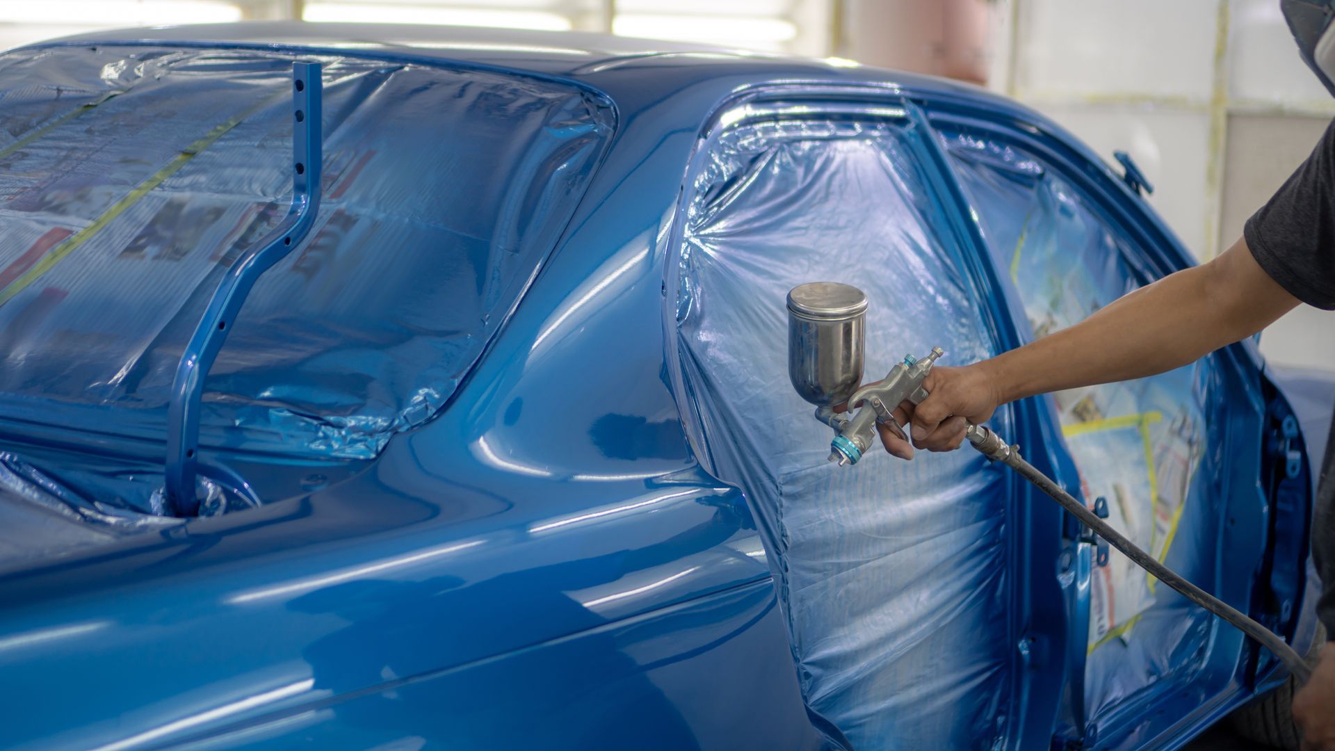 Person spray painting a blue car in a workshop, using a spray gun.