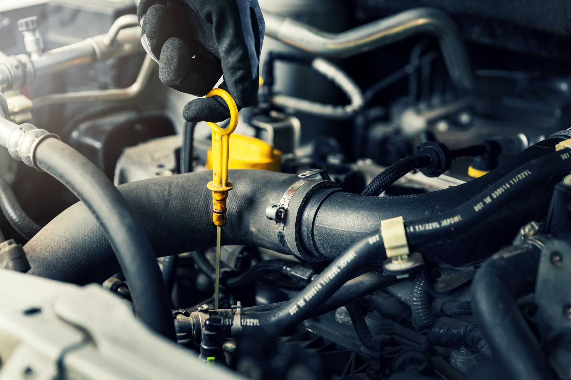 Gloved hand checking engine oil level with a yellow dipstick in a car engine compartment.