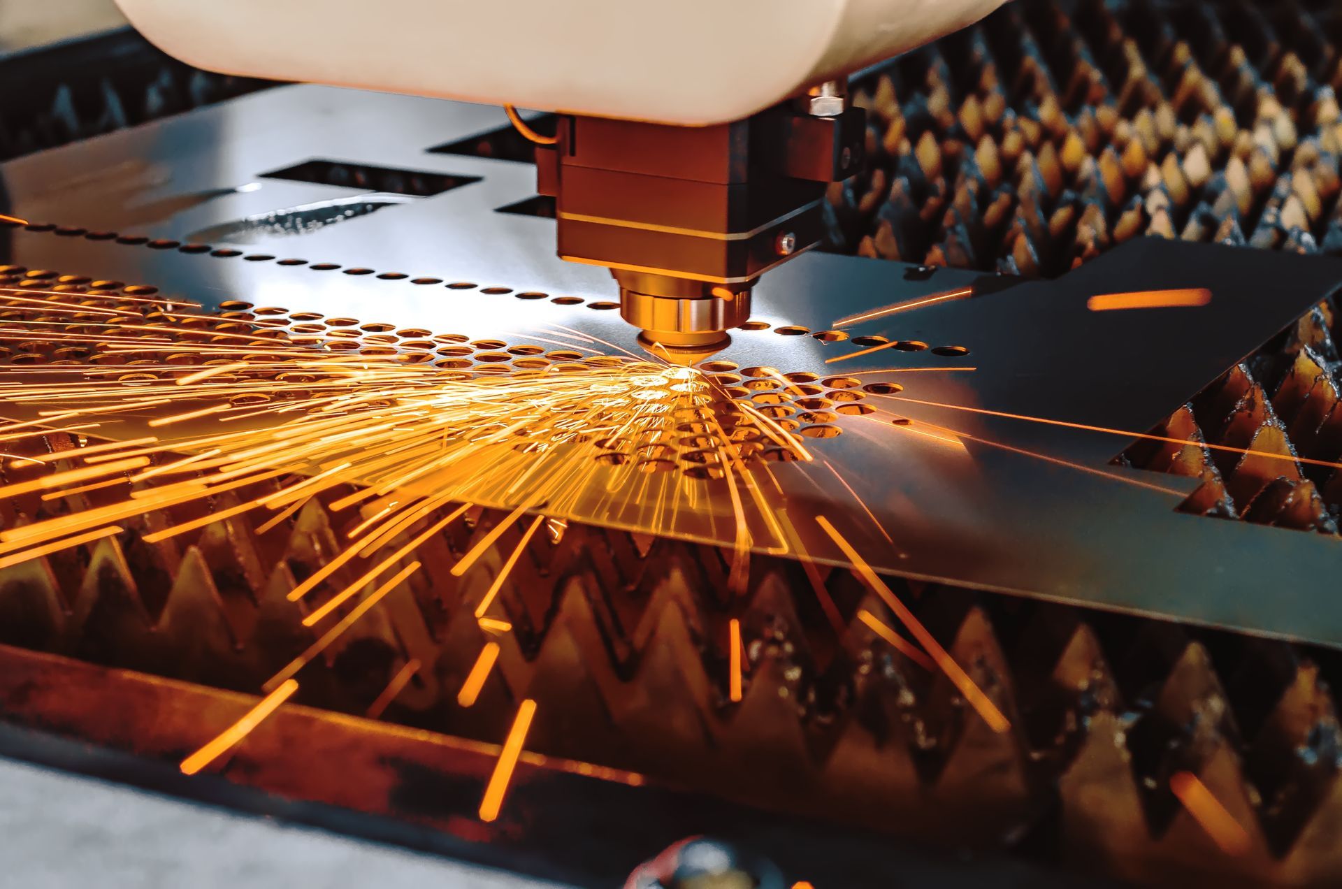 Laser cutter cutting metal sheet, orange sparks flying.